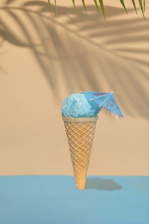 Blue ice cream in cone with cocktail parasol on beach background