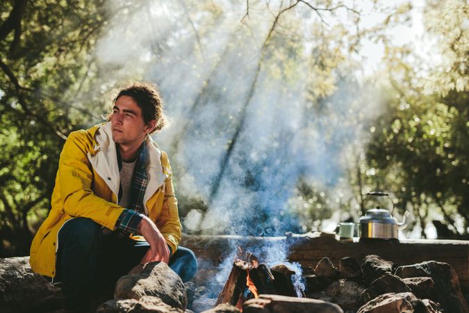 Man on camping trip sitting beside a bonfire in a forest