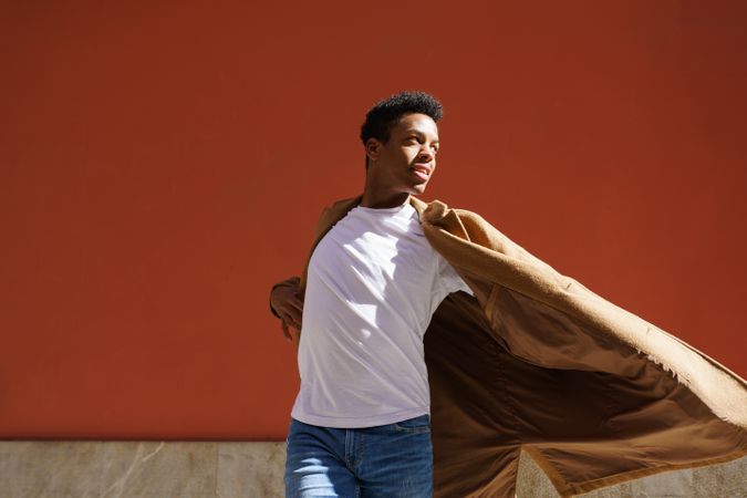 Black male in camel coat with his arms outstretched