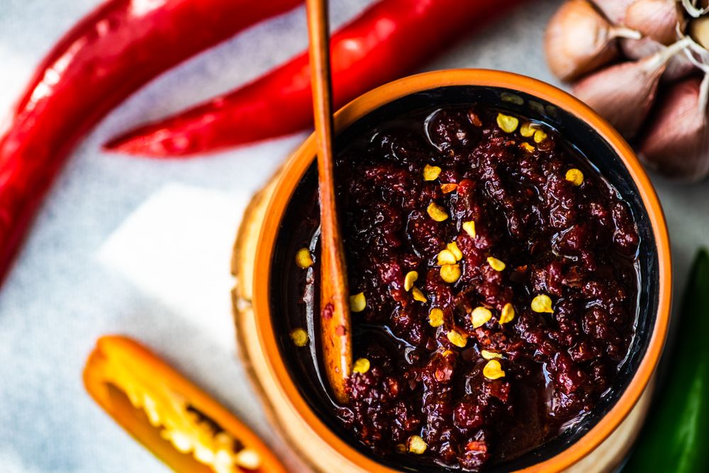 Top view of traditional Georgian sauce Adjika with spicy peppers, with wooden spoon and copy space
