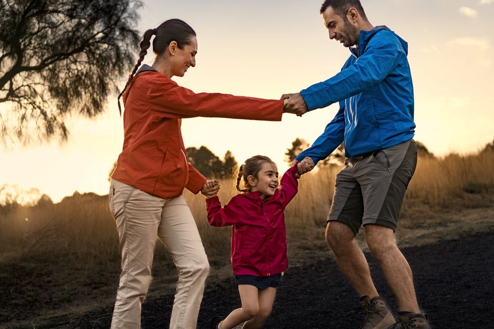 Happy family playing and dancing together in a field at sunset.
