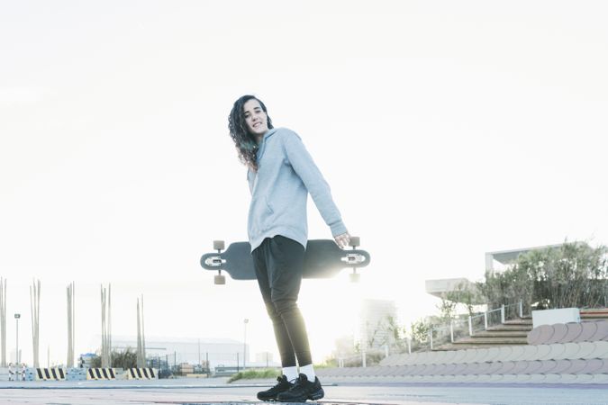 Low angle view of a teenage girl looking at camera while holding a longboard and smiling