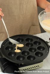 Hands spooning batter into bubble waffle maker for Japanese dish 42yZ75