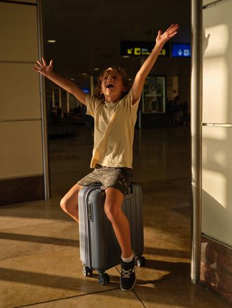 Excited boy sitting on suitcase in airport