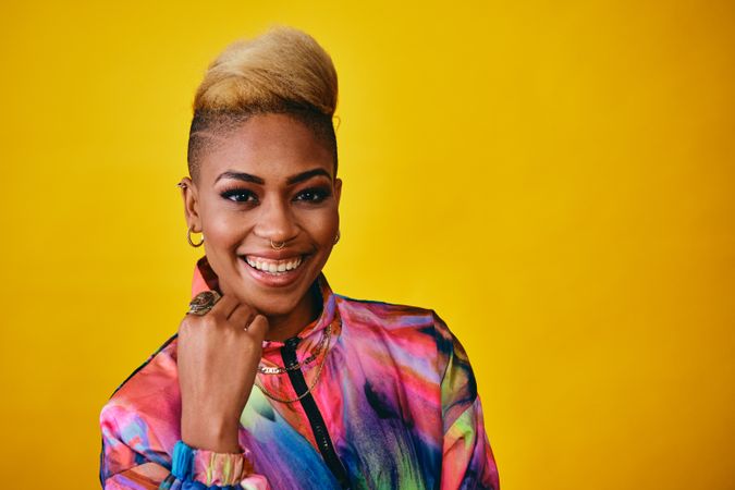 Studio shot of happy Black woman in bright 80s windbreaker jacket with hand on chin with copy space