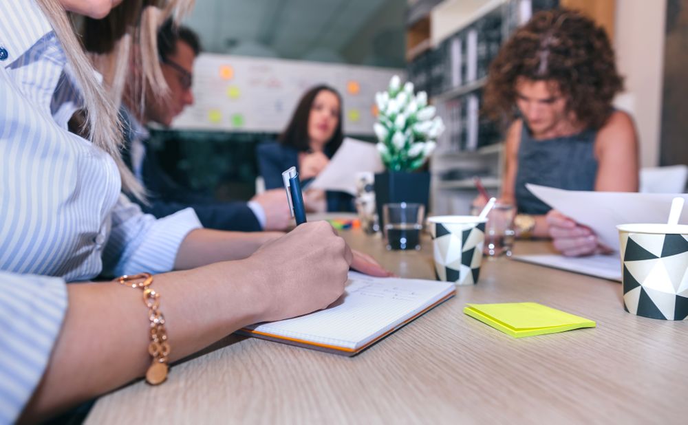Woman writing notes in a meeting with team