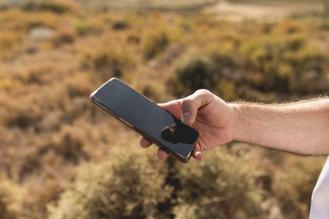 A man's hand, uses smartphone to look for something during a walk in the countryside