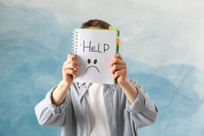 Male holding up notebook with the word “help”