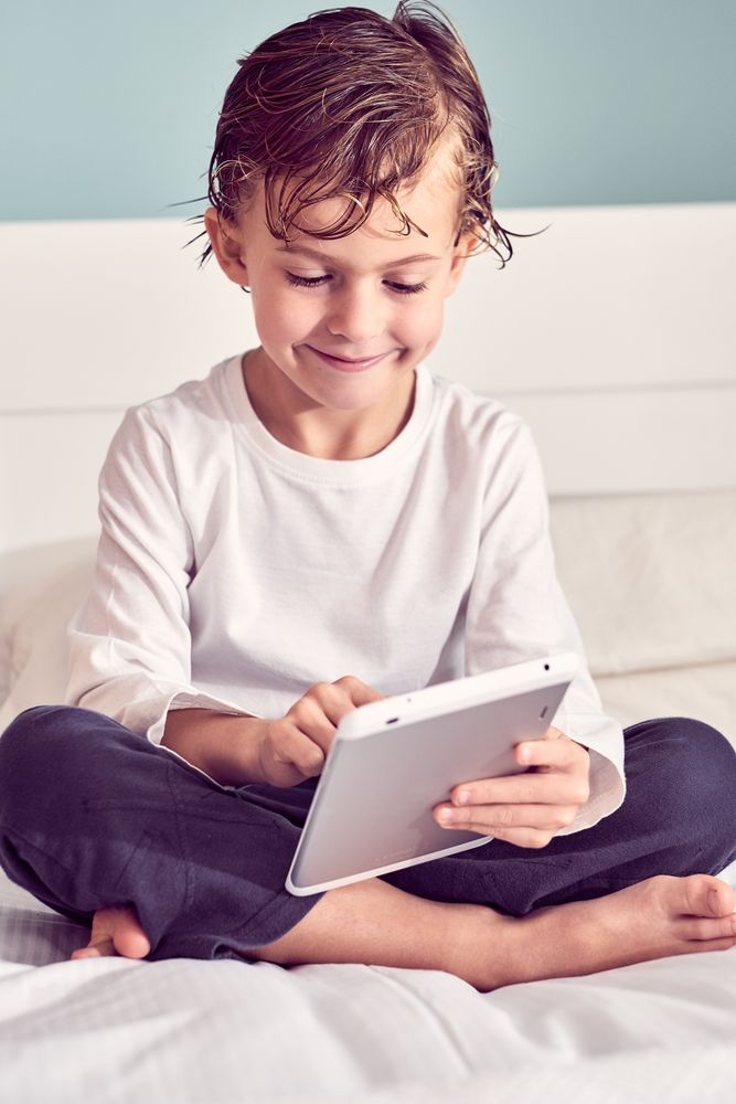 Smiling boy with wet hair browsing tablet on bed