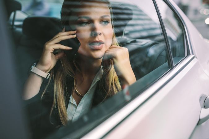 Young businesswoman sitting on back seat of a car and talking on phone
