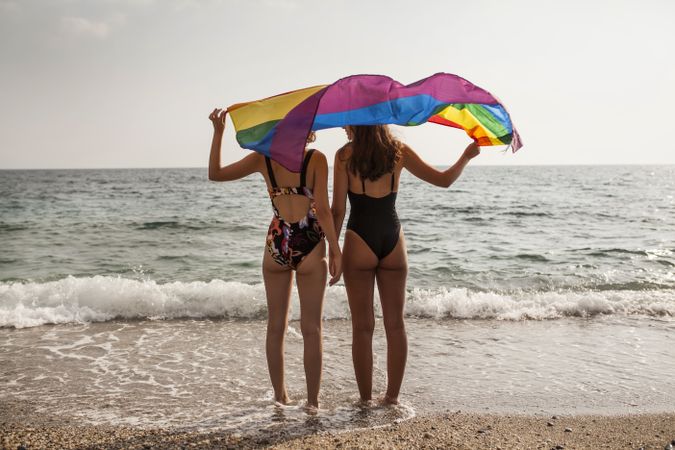 Females standing with rainbow flag on seashore