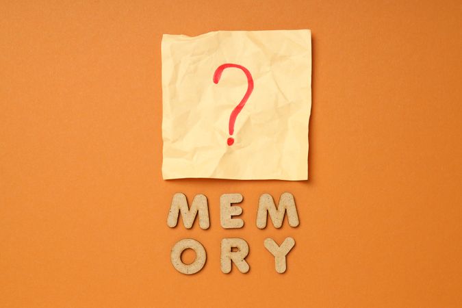 The word “Memories” written in cork below post it note on dusty orange background