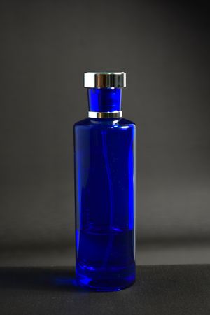 Blue perfume bottle in grey studio with space for text