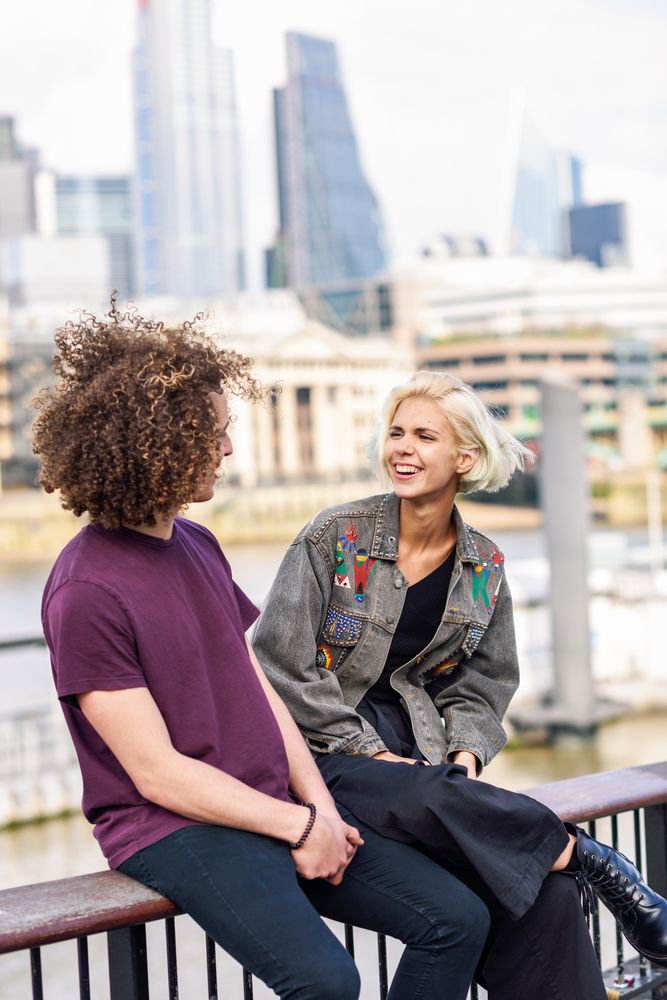 Blonde female and curly haired male chatting while sitting on fence over river