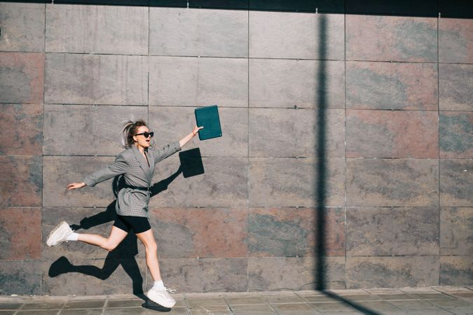 Woman joyfully jumping along wall with tablet