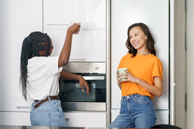 Two women talking while leaning on the fridge with coffee
