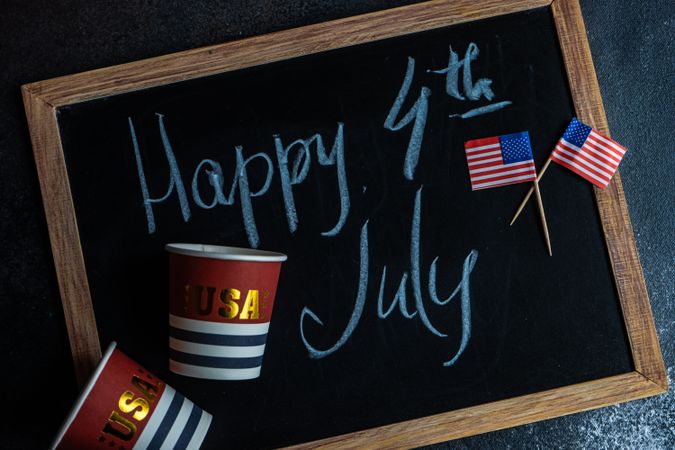Chalkboard with the words "Happy 4th of July" with American flags and USA cups