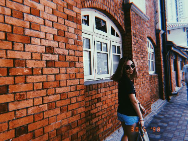 Woman in dark shirt and blue denim shorts walking beside brown brick wall