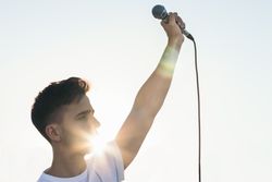 singer with the arm raised holding a microphone with sunlight reflects