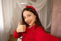 Teen girl smiling giving thumbs-up gesture in selfie photo.