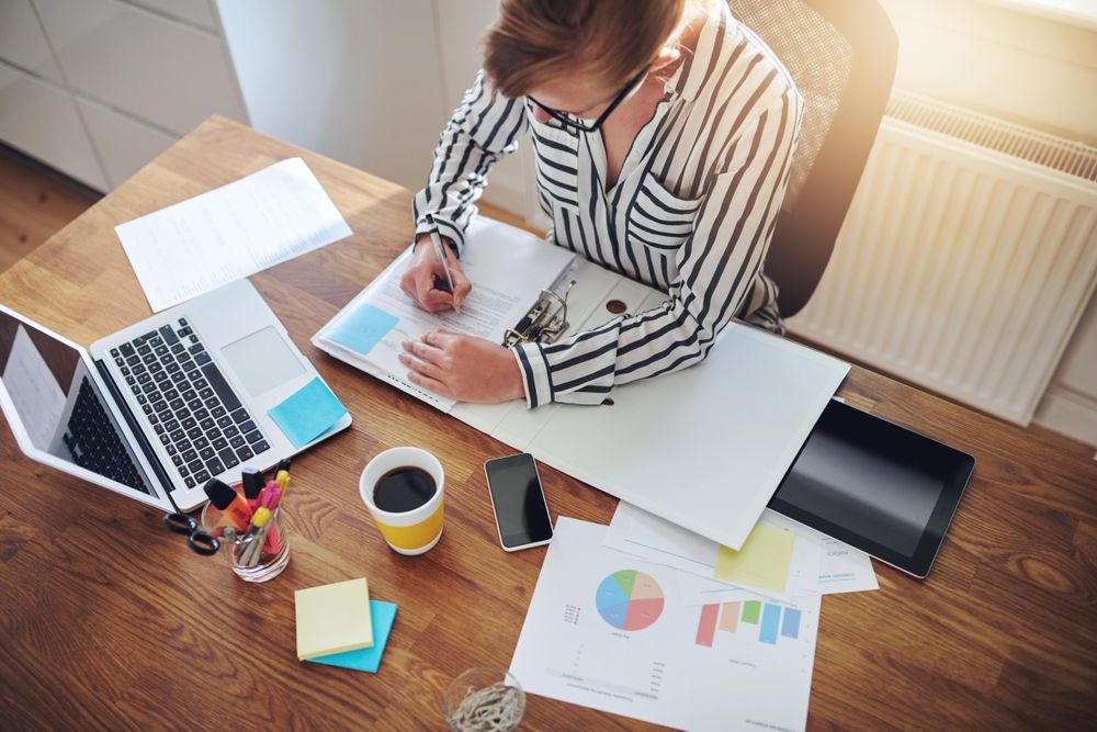 Top view of woman taking notes from laptop in home office with coffee