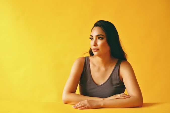 Solemn Hispanic woman looking wistfully away from camera and sitting in yellow room, copy space