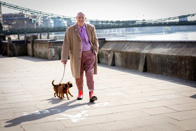 Content older man walking by river with two small dogs