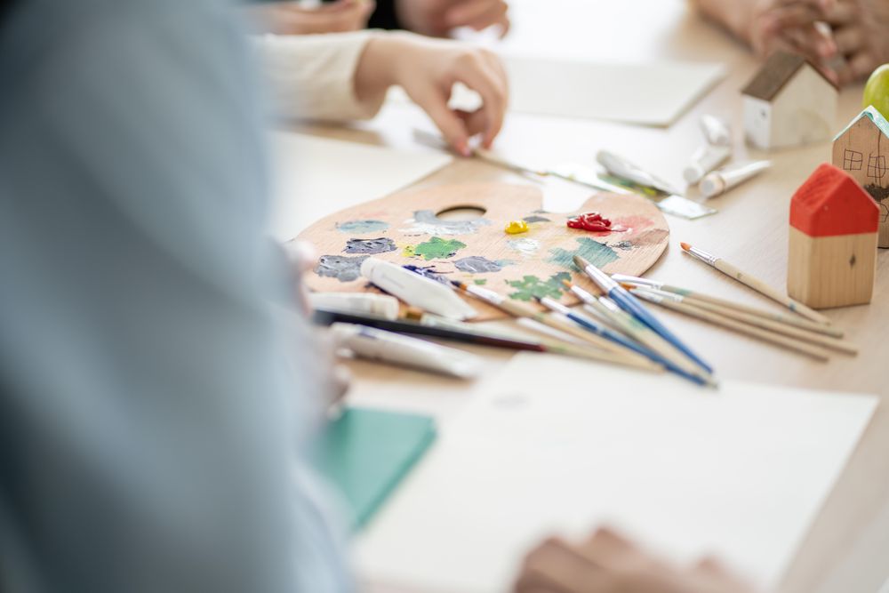 Student hands with paint and brushes on classroom table