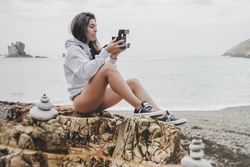 Woman with camera on shore near stones and water