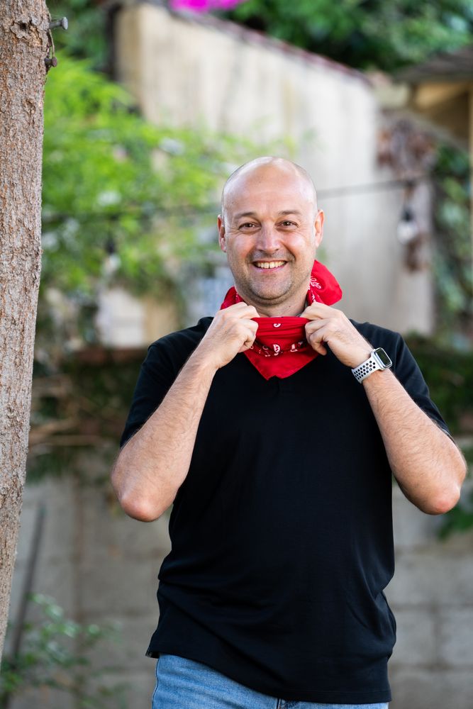 Man smiling and looking at camera with red bandana around his neck standing outside