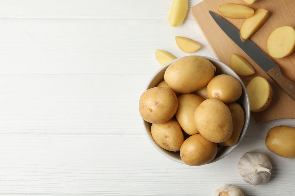 Top view of bowl full of potatoes on kitchen counter with garlic and knife, copy space