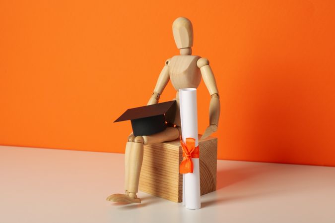 Wooden statuette of a man with a graduation hat and diploma.