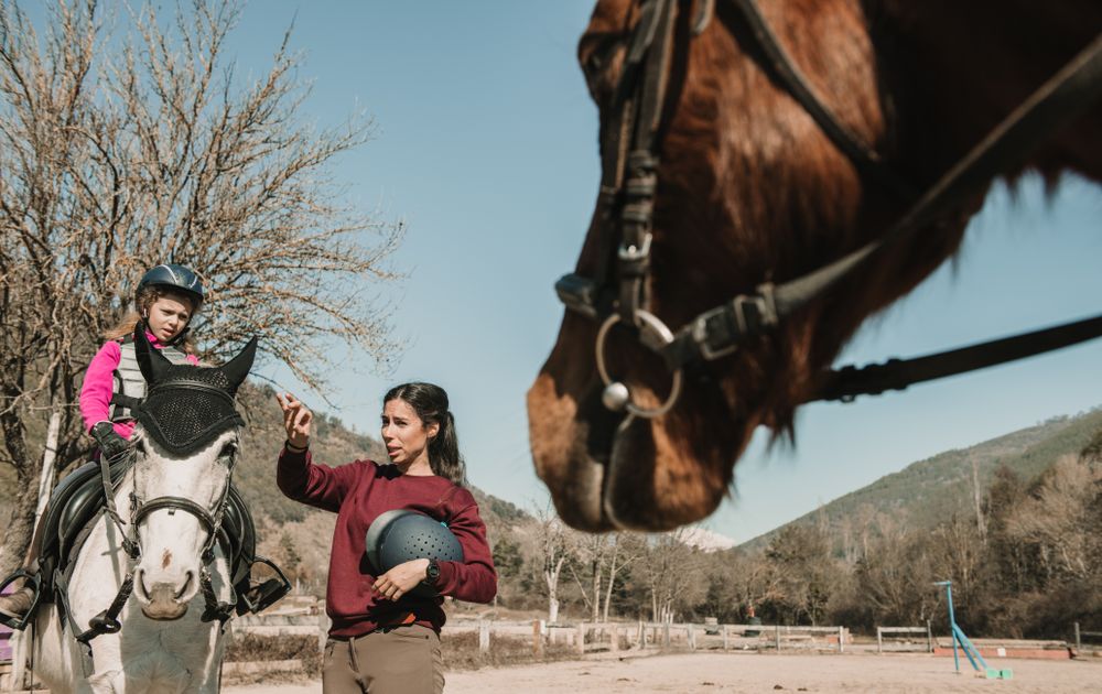 Young woman teaching girl to ride horse