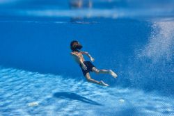 Unrecognizable barefoot boy swimming in blue pool