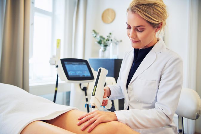 Female cosmetologist performing treatment on legs