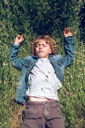 Cute preteen boy lying on green meadow and enjoying daydream