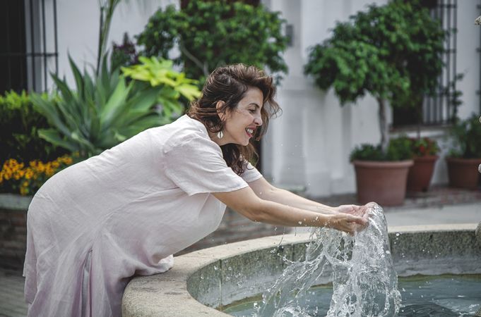 Joyful female splashing water in city fountain