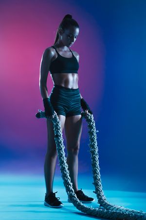 Fitness woman standing holding two battle ropes during workout