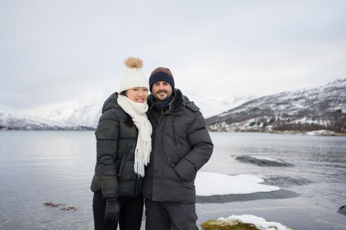 Happy friends on pond shore against highland in winter