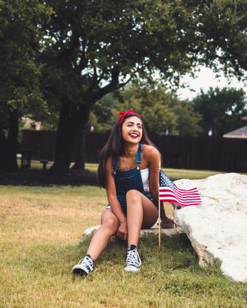 Woman smiling and  sitting on rock beside US flag