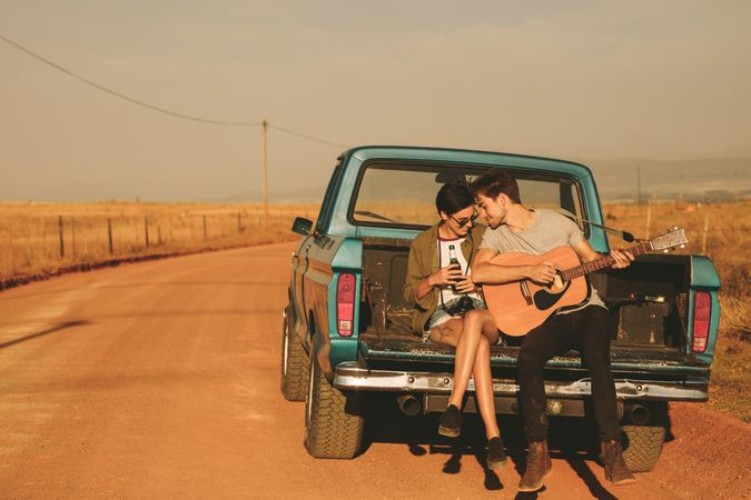 Couple sitting in back of pickup truck enjoying road trip in country side
