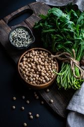 Bowl of garbanzo beans and sesame seeds next to arugula 