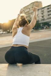 Strong woman with arms raised doing a squat or stretch outdoors at sunset