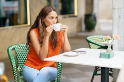 Latina woman drinking coffee sitting relaxed on a pavement cafe