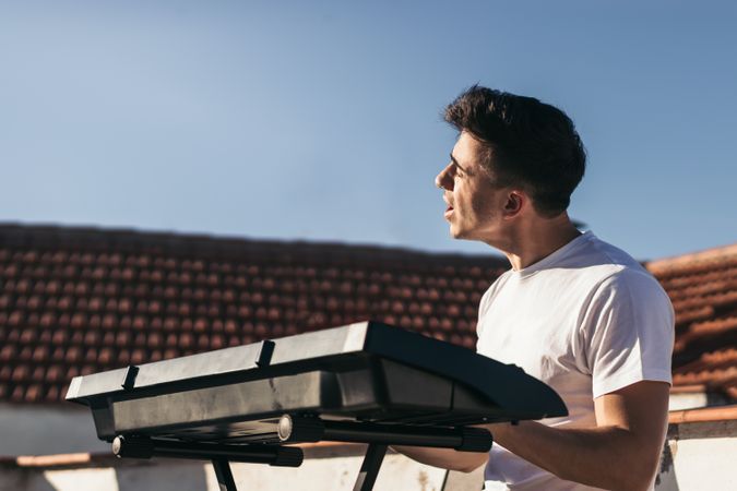 man playing a music keyboard and singing on a rooftop