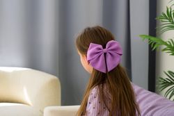 Girl with purple bow in hair sitting by window.