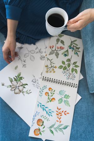 Young anonymous woman with coffee looking album with pictures