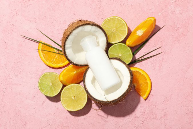 Coconut, fruits and cosmetics on pink background, top view