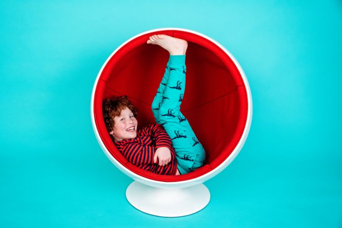 Portrait of boy in red shirt sitting in round globe designed chair