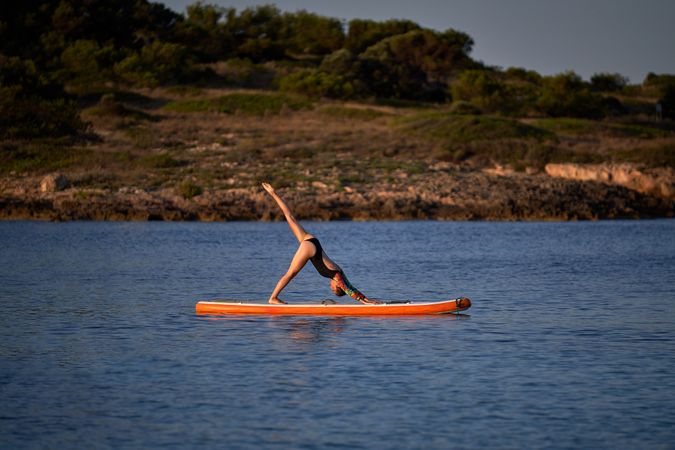 Sportswoman taking Downward Facing Dog pose on paddleboard in se